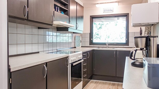 Une cuisine moderne avec des meubles de couleur sombre, une cuisinière en acier inoxydable, une fenêtre offrant une belle vue et une machine à café.
