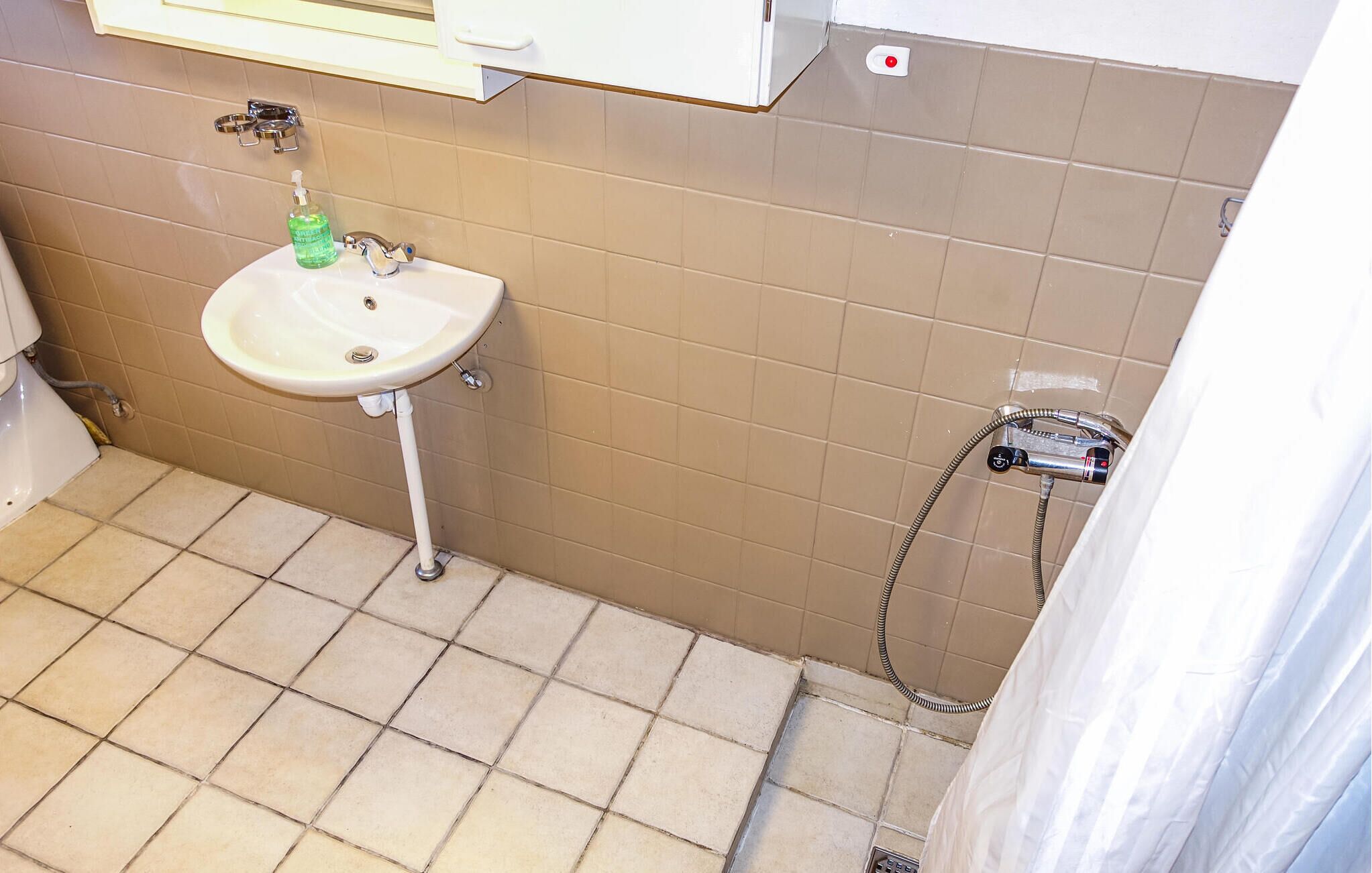 Une salle de bain avec un lavabo blanc, une douchette à main et un porte-serviettes.