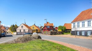 Une vue de rue avec des maisons traditionnelles, un ciel dégagé et une route où circulent des voitures.