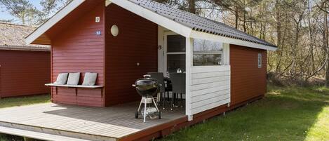 Une petite cabane avec une terrasse, un barbecue et un banc.