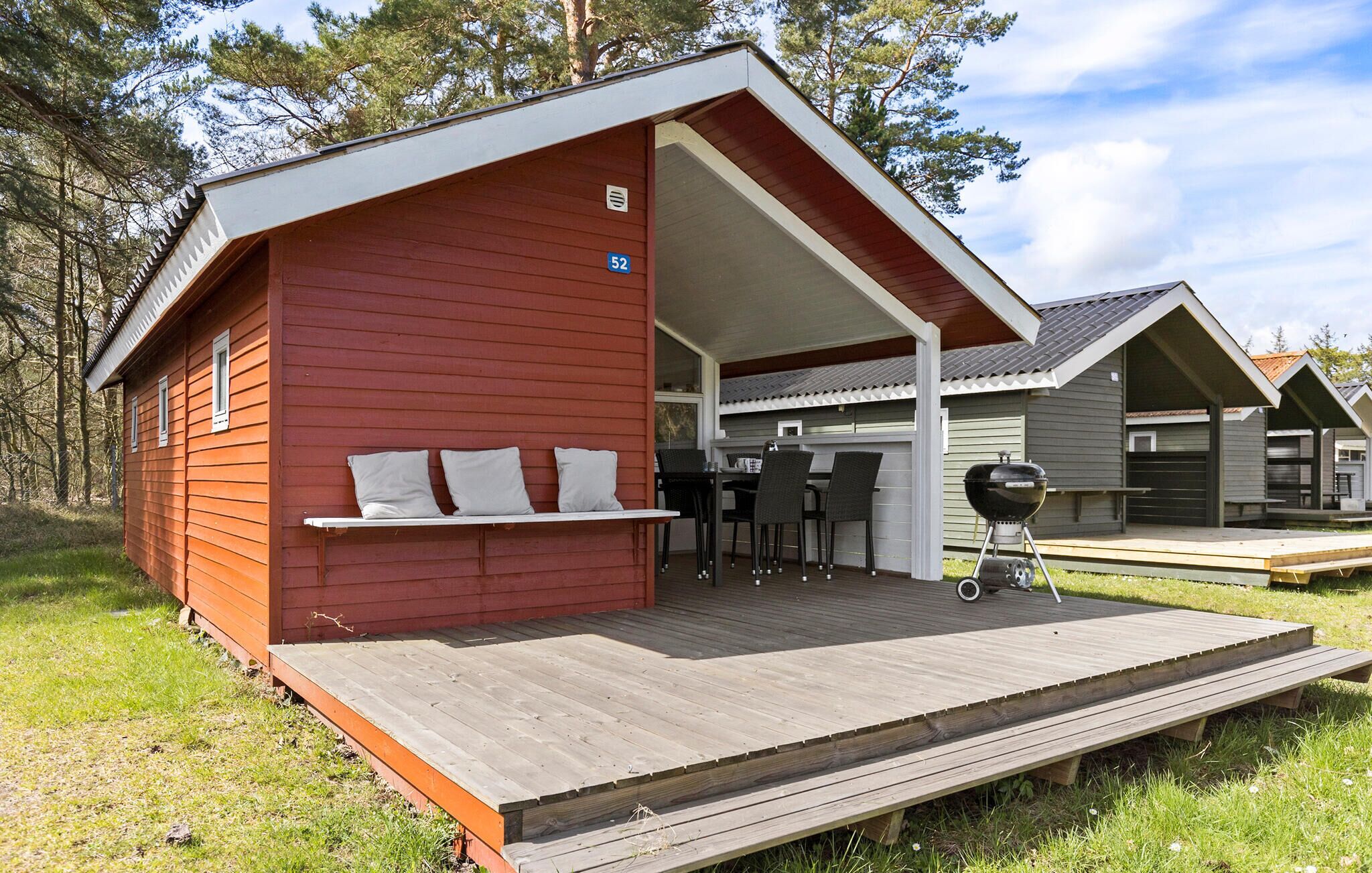 Une cabane rouge dotée d’un patio couvert, d’un barbecue et d’une petite table avec des chaises.