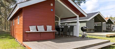 Une cabane rouge dotée d’un patio couvert, d’un barbecue et d’une petite table avec des chaises.