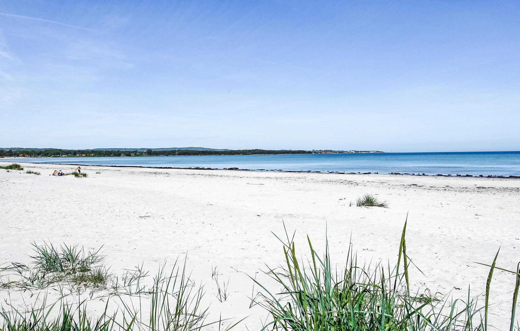 A beach with white sand and sparse vegetation in the foreground.