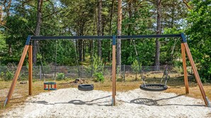 A swing set in a sandy area with a chain-link fence and trees in the background.