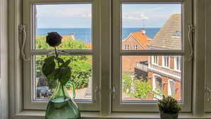A window with a view of a coastal town, a rose in a vase, and a small potted plant. - 2 bedroom nice apartment in Gudhjem (Gudhjem)