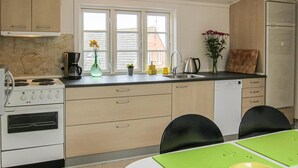 A kitchen with a stove, sink, and refrigerator. There is a window with a view of buildings outside. - 2 bedroom nice apartment in Gudhjem (Gudhjem)