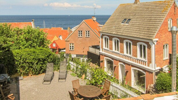 A coastal town with red-roofed buildings, a paved courtyard with outdoor seating, and a view of the sea. - 2 bedroom nice apartment in Gudhjem (Gudhjem)