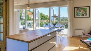 Eine moderne Küche mit einer großen Kochinsel, einem Essbereich mit Stühlen und einem Tisch, und Blick ins Freie.