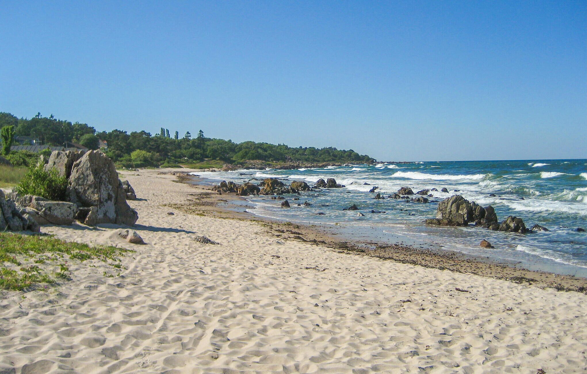 A sandy beach with rocky outcrops and waves crashing onto the shore.