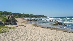 Ein sandiger Strand mit Felsformationen und brechenden Wellen.