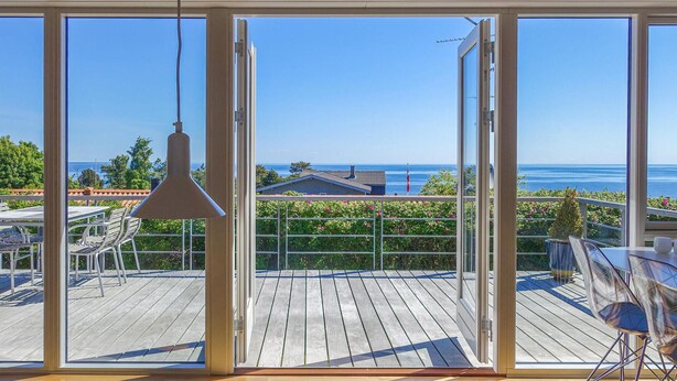 Ein Balkon mit Holzboden, einer hängenden Pendelleuchte und Blick auf das Meer und Gebäude.