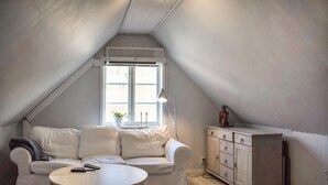 Una habitación acogedora en el ático con un sofá blanco, una pequeña mesa redonda y un armario.