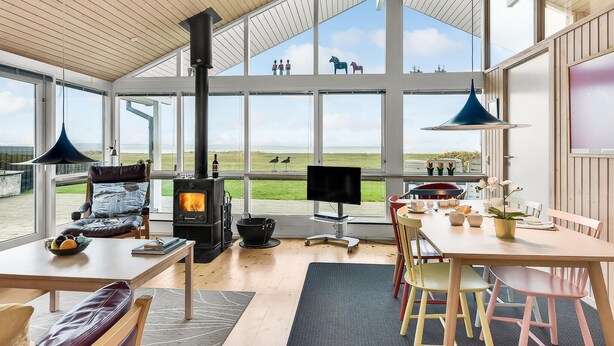 Een ruime kamer met een groot raam, een open haard, een eettafel en een televisie.