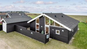 Een modern zwart gebouw met een schuin dak, grote ramen en uitzicht op zee.