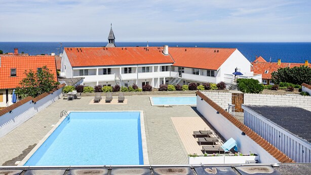 A hotel with a swimming pool, outdoor seating, and a view of the sea.