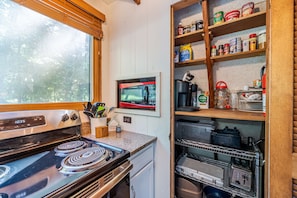 A compact kitchen with a stove, microwave, and shelves stocked with various food items. - Lakefront A-Frame · Hot Tub · Paddle Pontoon Boat (Innsbrook)