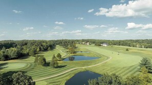 A golf course with multiple ponds, a clubhouse, and surrounding wooded areas.