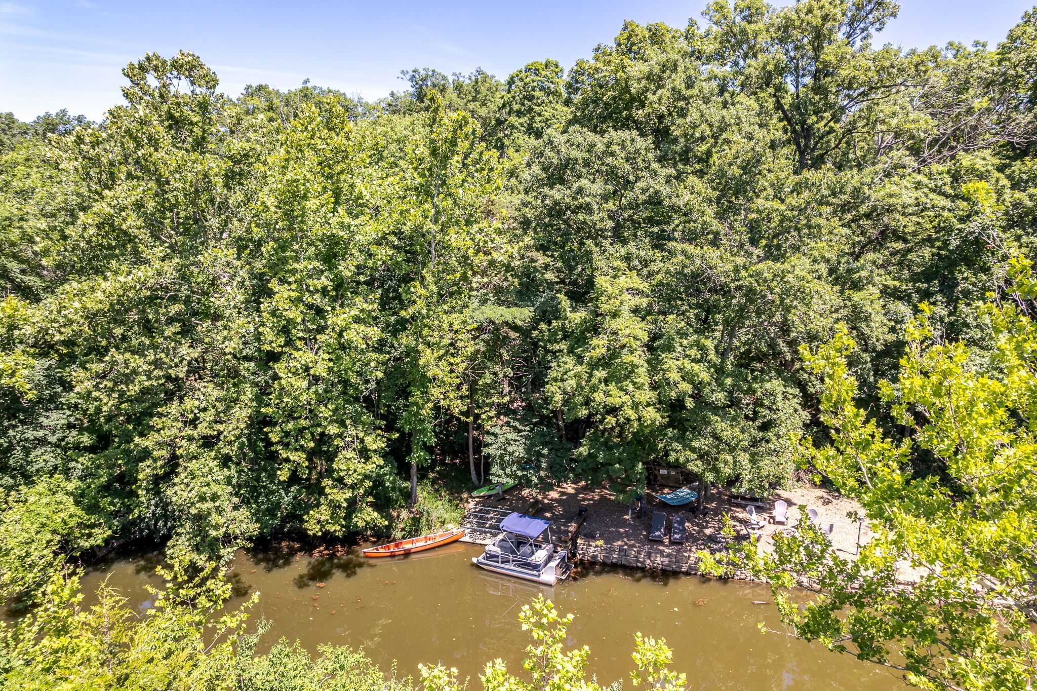 A river surrounded by dense forest with a dock and chairs.