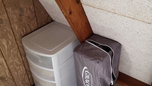 Huoneen nurkka, jossa on valkoinen muovinen säilytysyksikkö ja harmaa GRACO-kassi. Taustalla on kuvioitu seinä ja puupalkki.