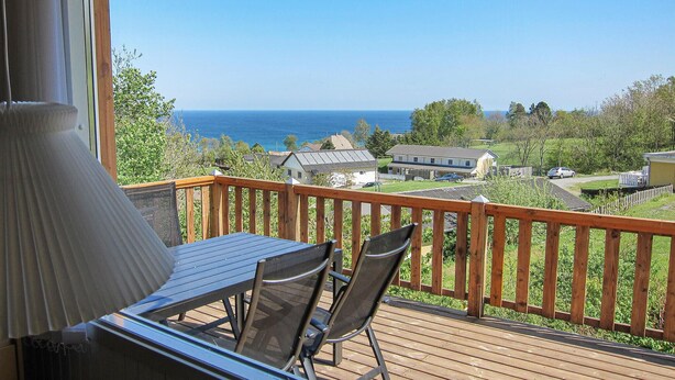 A wooden deck with a table and chairs, overlooking a residential area and the sea. - 2 bedroom awesome home in Allinge (Allinge)