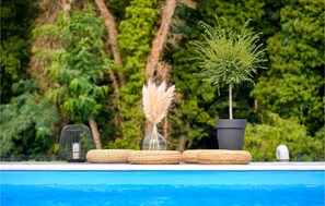 Un décor au bord de la piscine, avec un petit arbre, un vase contenant de l’herbe des pampas et un objet décoratif posé sur une étagère.