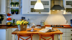 Una cocina con armarios blancos, una isla de madera, una lámpara colgante y diversos utensilios de cocina.
