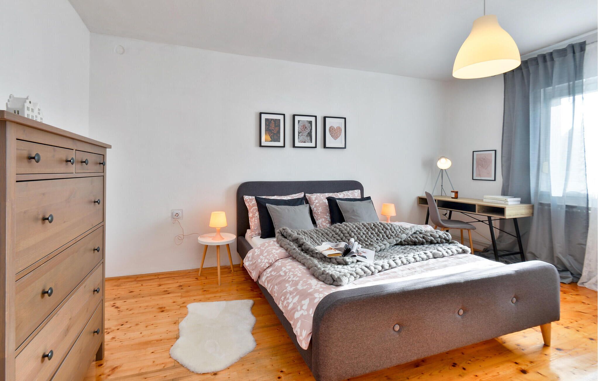 A bedroom with a bed, a desk, a chair, a dresser, and a lamp.