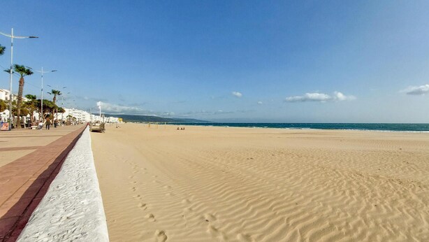 A wide sandy beach with a clear sky and a few people walking.