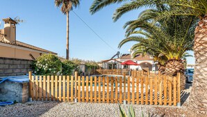 A residential area with a wooden fence, palm trees, and a house with a tiled roof.