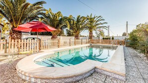 A swimming pool with a wooden fence, palm trees, and a red umbrella.