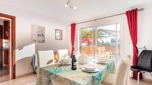 A dining area with a table set for two, a bottle of wine, and a tropical-themed tablecloth.