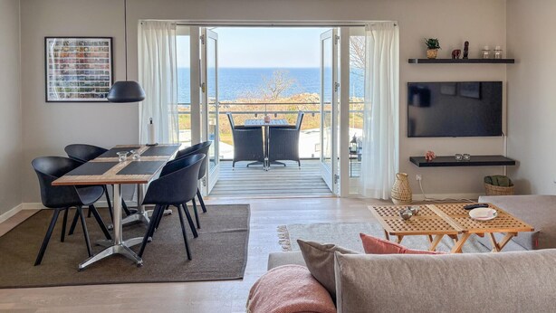 Un salon avec un canapé, une table à manger et des chaises, un téléviseur et un balcon avec vue sur la mer.