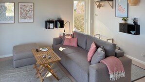 Un salon moderne avec un canapé gris, une table basse en bois et une petite table d’appoint. Deux étagères murales sont ornées d’objets décoratifs et d’une carte.