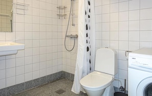 A bathroom with a toilet, a washing machine, and a shower.