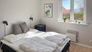 Une chambre à coucher avec un lit, un radiateur, une fenêtre ornée de plantes et une œuvre d’art encadrée accrochée au mur.