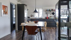 Una cocina moderna con zona de comedor, que cuenta con una isla grande, sillas de madera y una lámpara colgante.