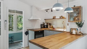 Eine moderne Küche mit Holzarbeitsplatte, einem eingebauten Ofen und einer Spüle. Über der Arbeitsfläche hängen Pendelleuchten und ein Fenster mit Blick auf Grünfläche.
