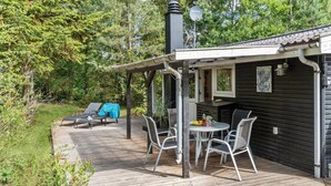 Eine Holzterrasse mit Sitzgelegenheit im Freien, einem überdachten Bereich und Blick auf einen bewaldeten Hügel.