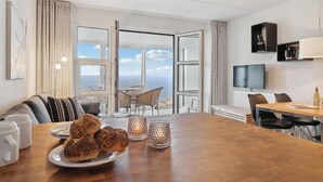 Ein modernes Hotelzimmer mit einem großen Esstisch, einer Couch und Blick aufs Meer.