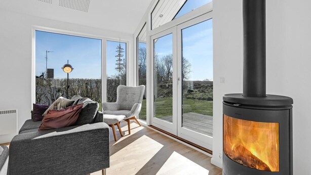 En moderne stue med en stor pejs, en sofa og en lænestol, der vender mod en glasdør til en have.