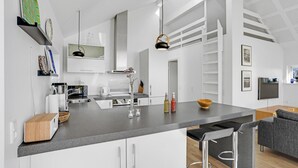 Et moderne køkken med en central ø, hvide skabe og et spiseområde med en grå sofa.