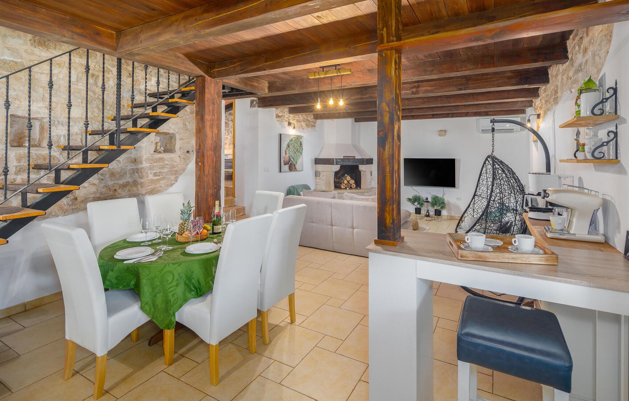Un espace repas agrémenté d’un escalier en bois, d’un mur en pierre et d’une cuisine moderne avec un fauteuil suspendu.