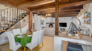 Zona pranzo con scala in legno, parete in pietra e cucina moderna con poltrona sospesa.