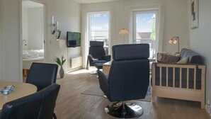 Ett modernt vardagsrum med en soffa, fåtöljer, ett matbord och en tv som är monterad på väggen.