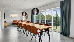 Et moderne spiseområde med et langt bord og stole, store vinduer og udsigt til det fri.
