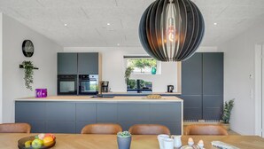 Et moderne køkken med en central ø, integrerede hårde hvidevarer og et spiseområde med et træbord og stole.