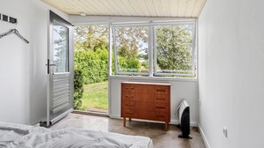 Une chambre à coucher avec un lit, une commode en bois, un radiateur et une fenêtre donnant sur un paysage verdoyant.