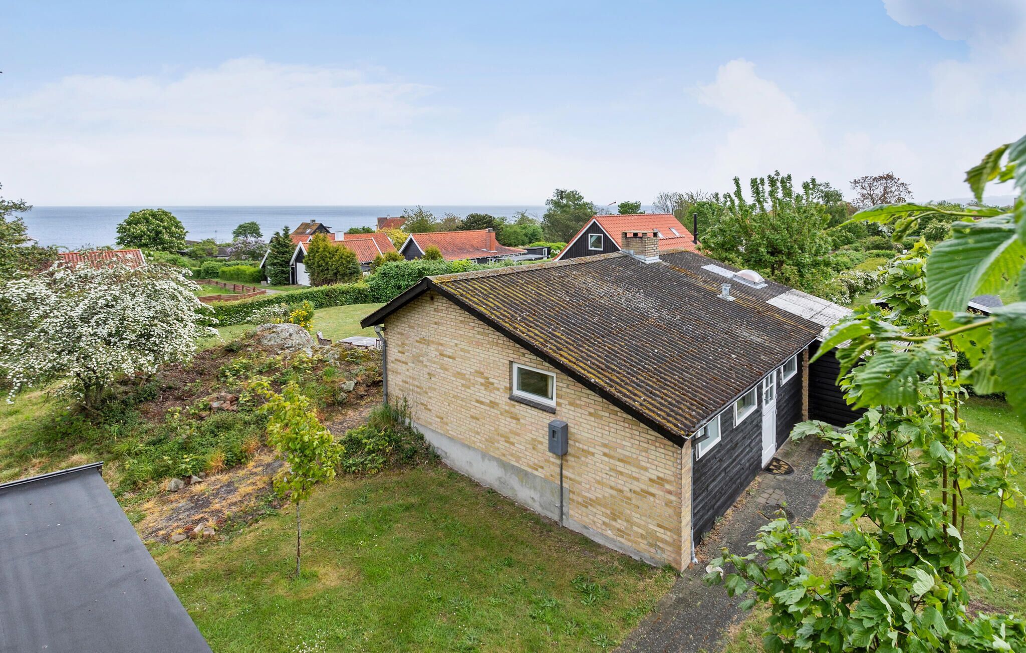 Ein kleines Haus mit Backsteinfassade und einem Ziegeldach, umgeben von einem Garten und Blick auf das Meer.