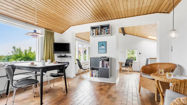 Un espace de vie moderne avec un plafond en bois, un coin repas comprenant une table et des chaises, une bibliothèque et un fauteuil en osier avec une petite table.