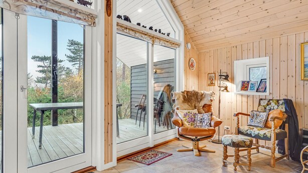 Ein gemütliches Interieur mit einem großen Schiebeglastür, die auf eine Terrasse führt, einem bequemen Ohrensessel, einem Holzstuhl und einem kleinen Tisch.